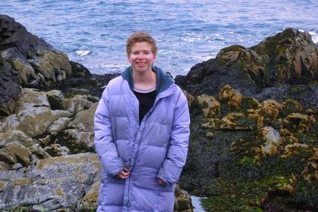 Kate Goldfield smiling on the rocky Maine coast in a lavender coat