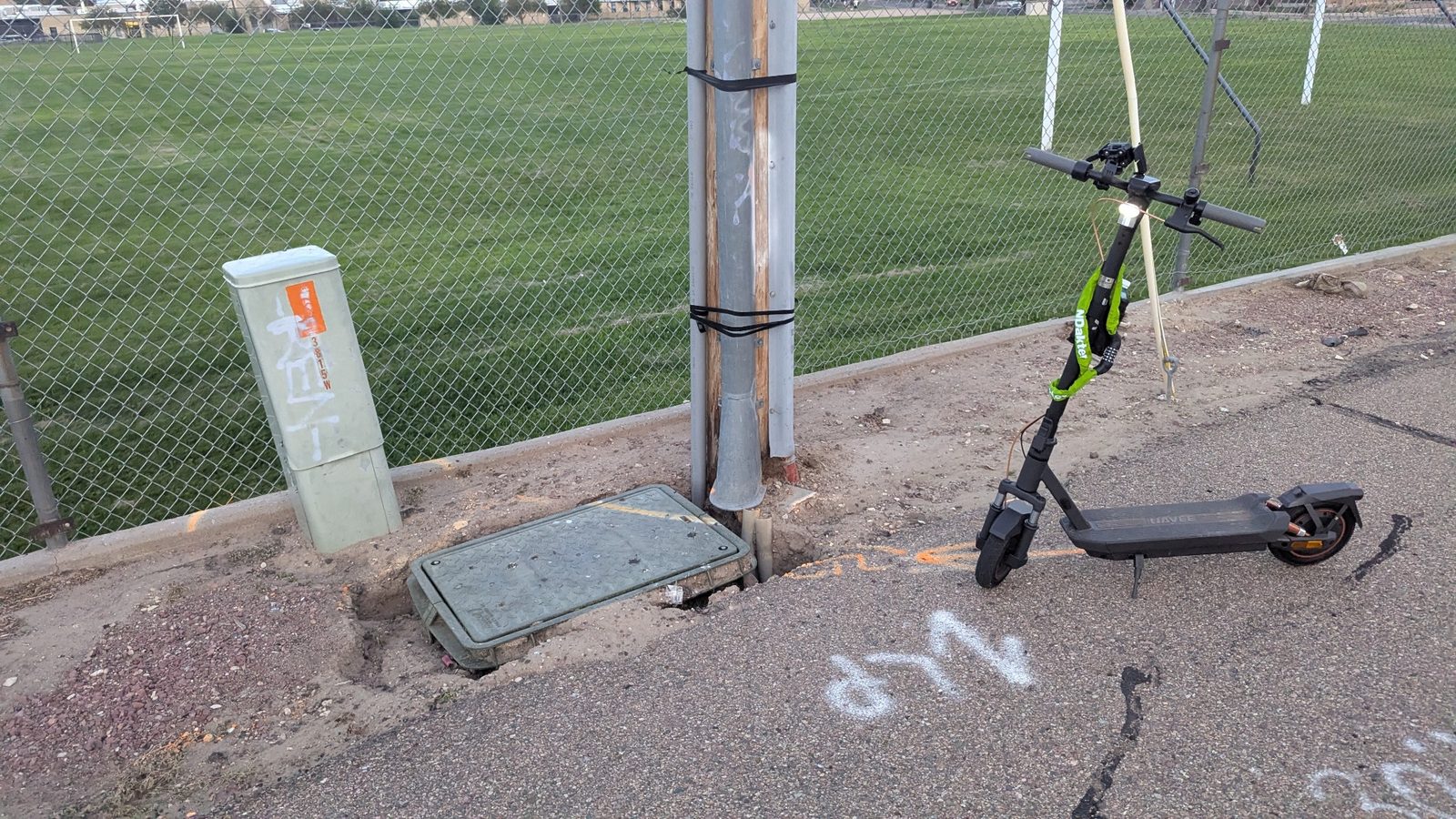 A black and lime scooter waits beside a utility cabinet and ground access cover.