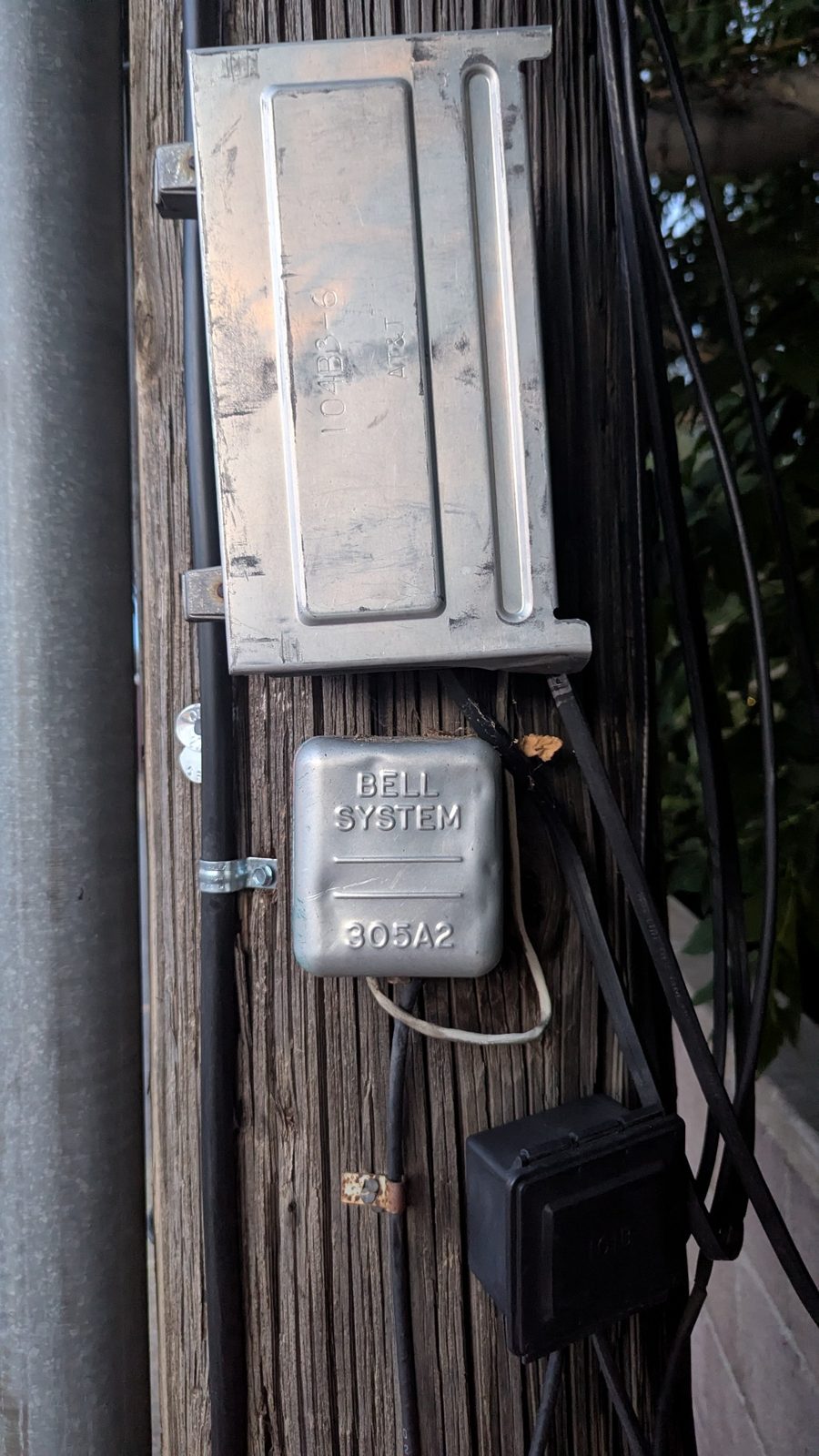 Two generations of telecom enclosures share one crowded utility pole.