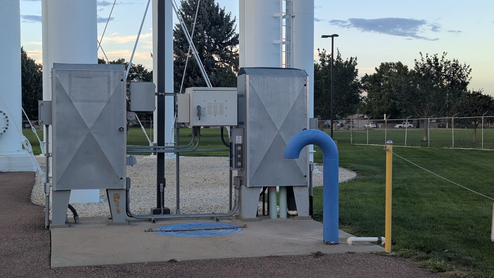 Pipes, cabinets, controls, and conduit gather beneath the water tower.