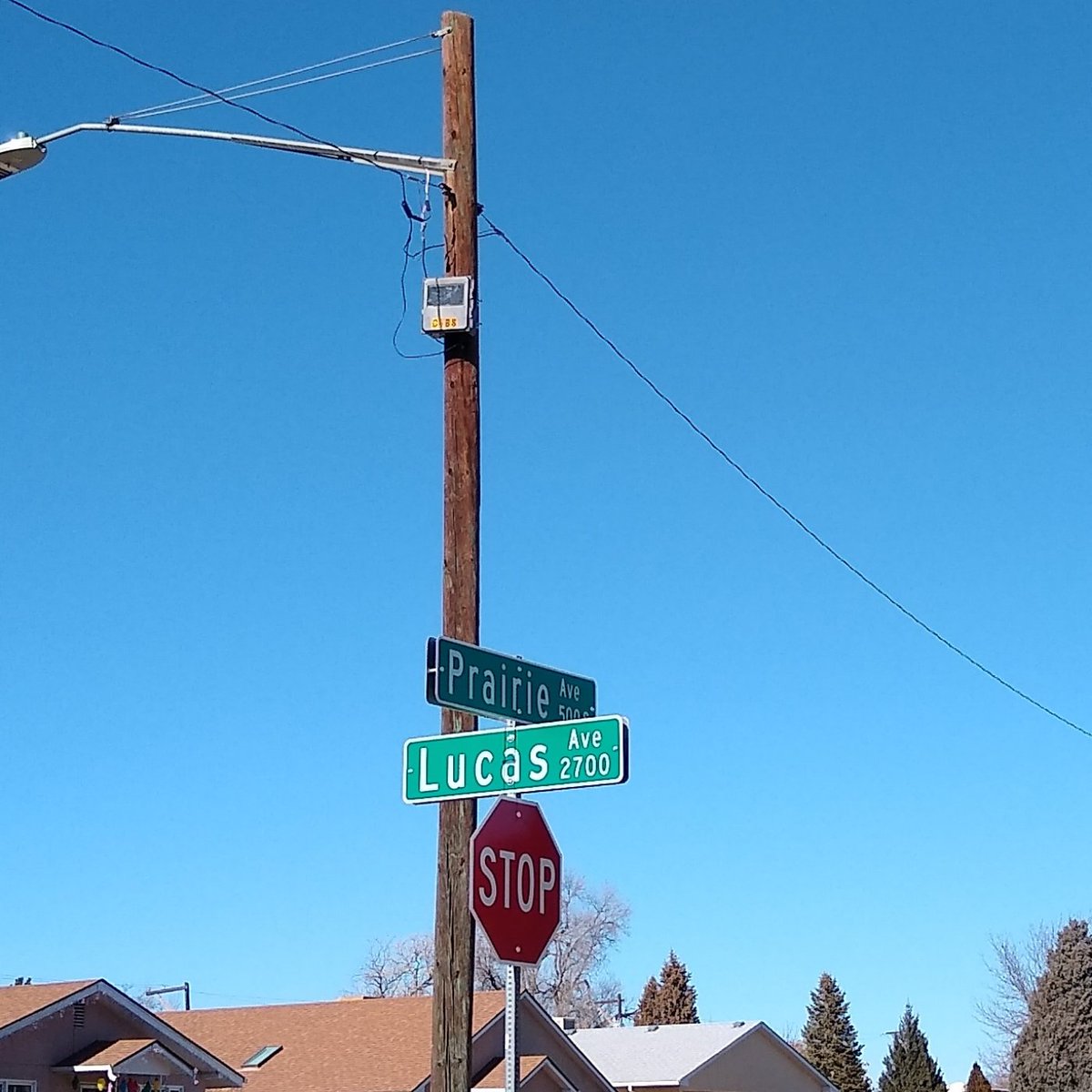 A small pale enclosure with darker upper panels mounted on a wooden utility pole above the Prairie and Lucas street signs
